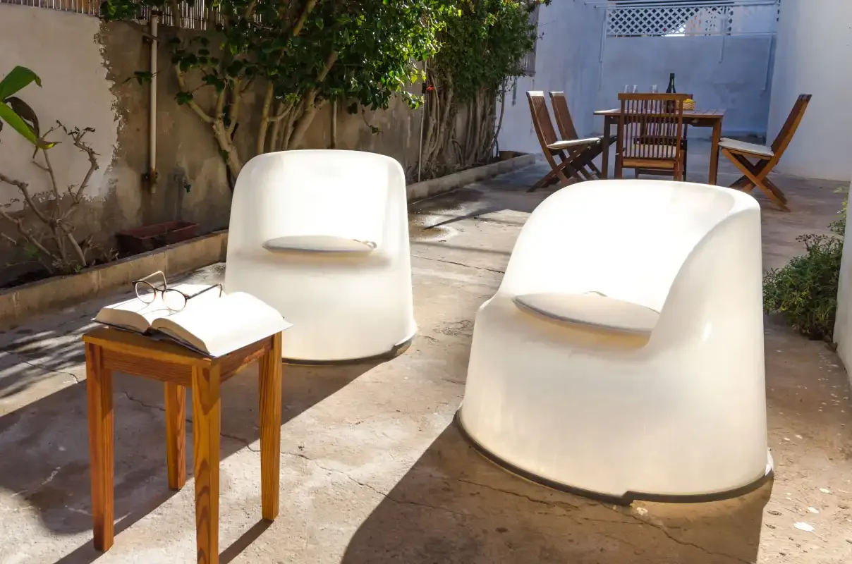 Un patio soleado tiene asientos blancos y una mesa de comedor de madera.