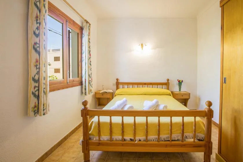 Un dormitorio con una cama de madera, ropa de cama amarilla y una ventana con cortinas estampadas.