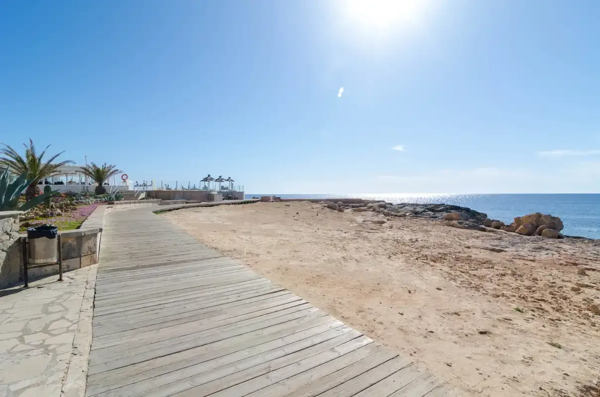 Un paseo marítimo bordea una playa de arena bajo un cielo despejado.