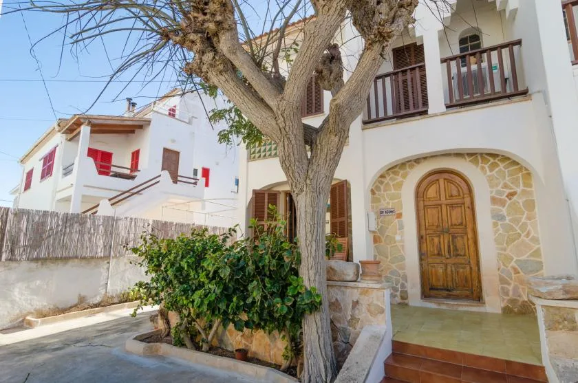 Entrada de una casa con puerta de madera, piedra y un árbol grande al frente.
