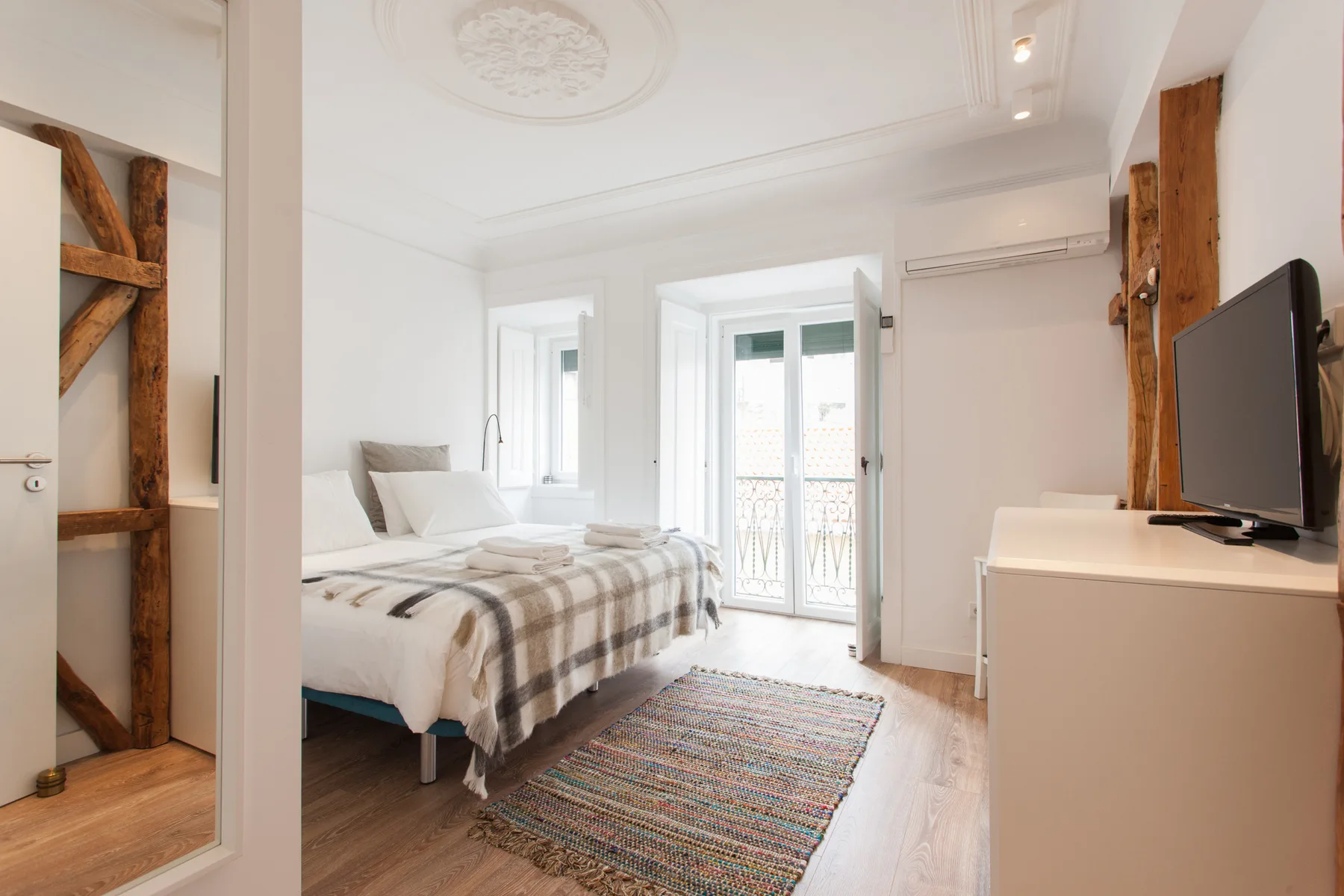 A bright bedroom with a bed, balcony doors, and a television on a dresser.