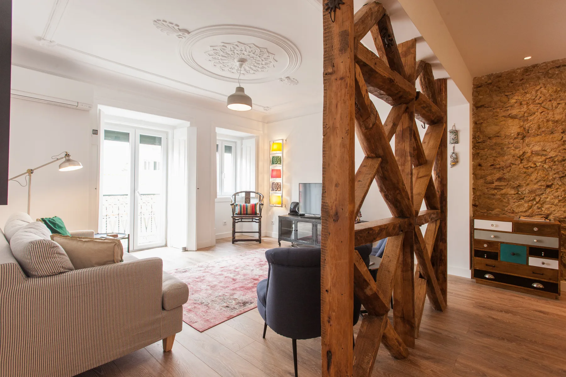 A bright living room with seating, tall windows, and exposed wooden beams.