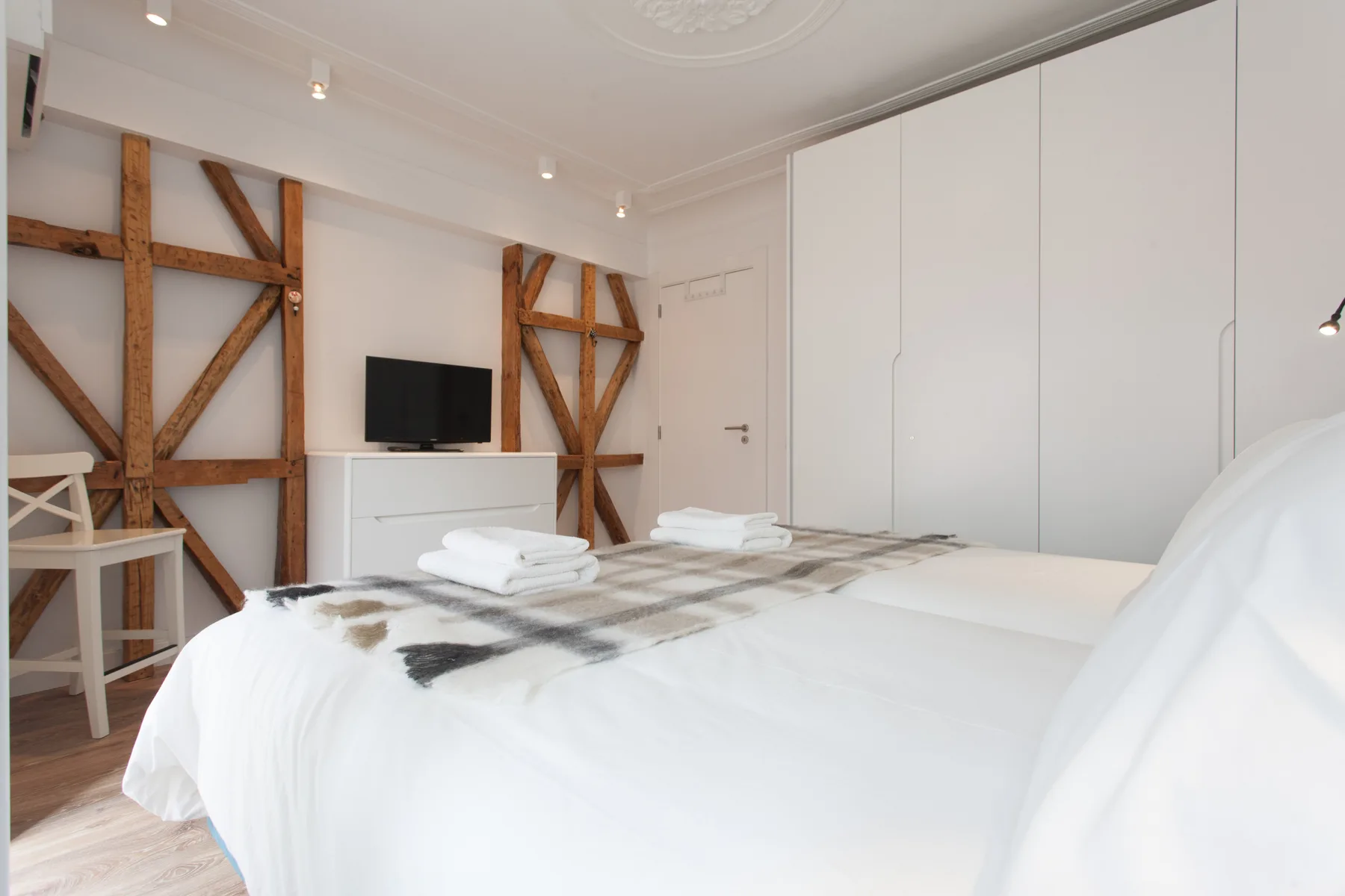 A bright bedroom with a white bed, folded towels, and exposed wooden beams.