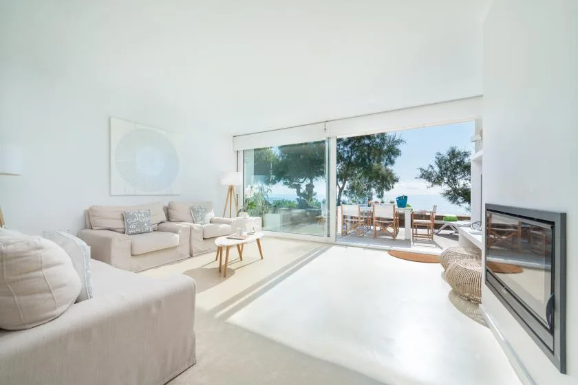 A bright living room opens through glass doors to a patio with outdoor seating.