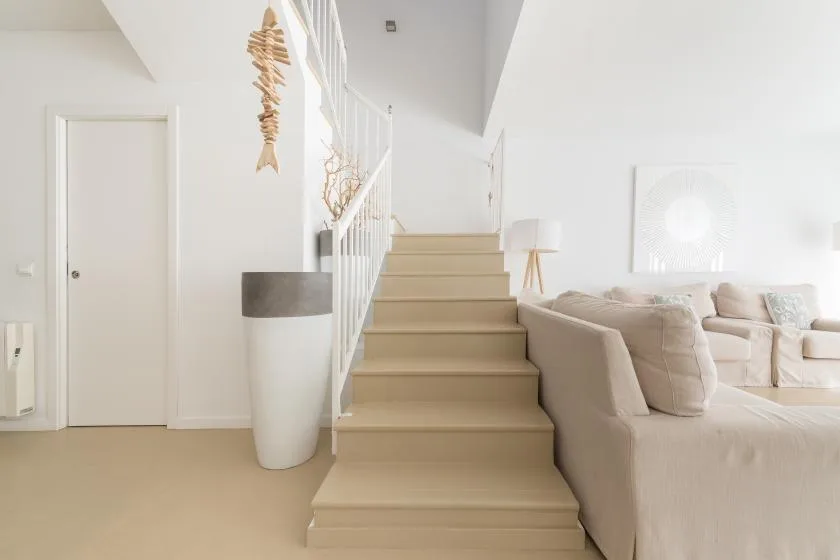 A bright living room with a staircase beside pale seating.