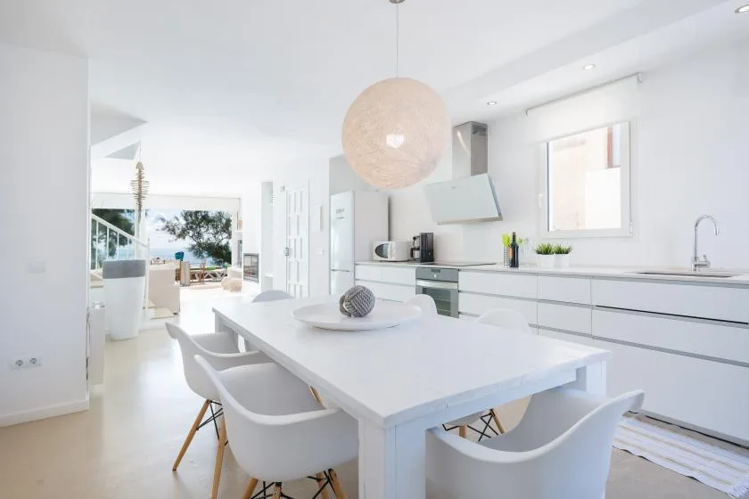 A bright white kitchen and dining area with a long table and large windows.