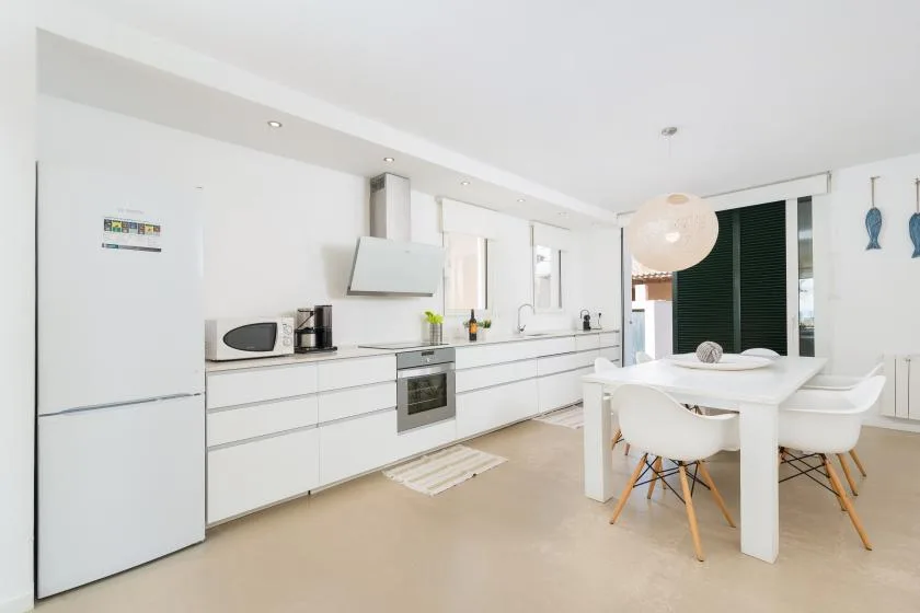 A bright modern kitchen with white cabinets, appliances, and a dining table.
