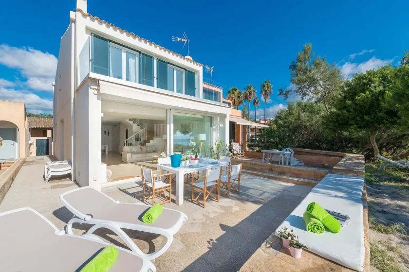 A modern house opens onto a sunny patio with outdoor dining and loungers.