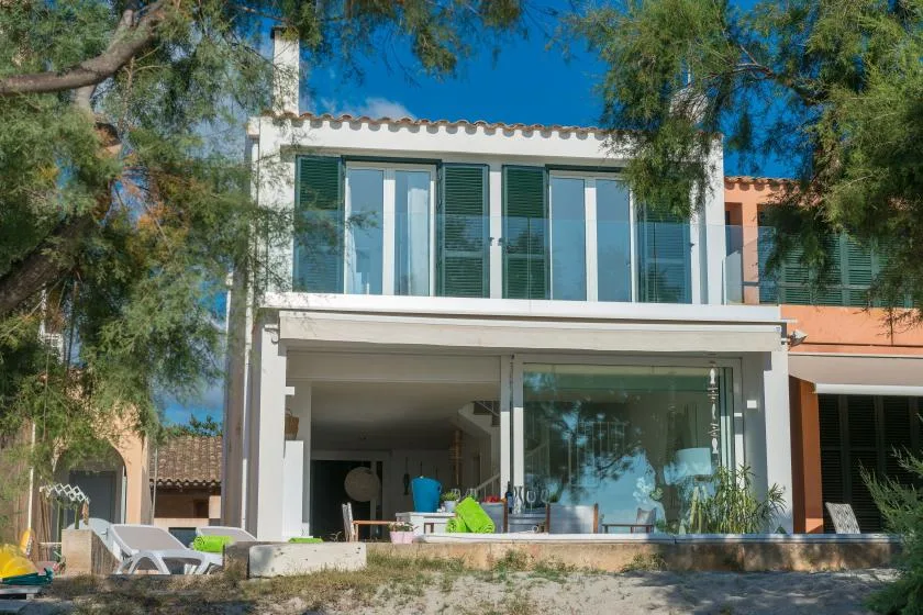 A two-story house with glass doors and windows, partly shaded by trees.