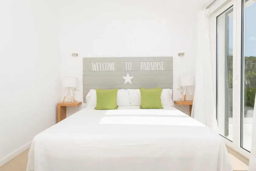 A bright bedroom with a neatly made bed and green accent pillows.