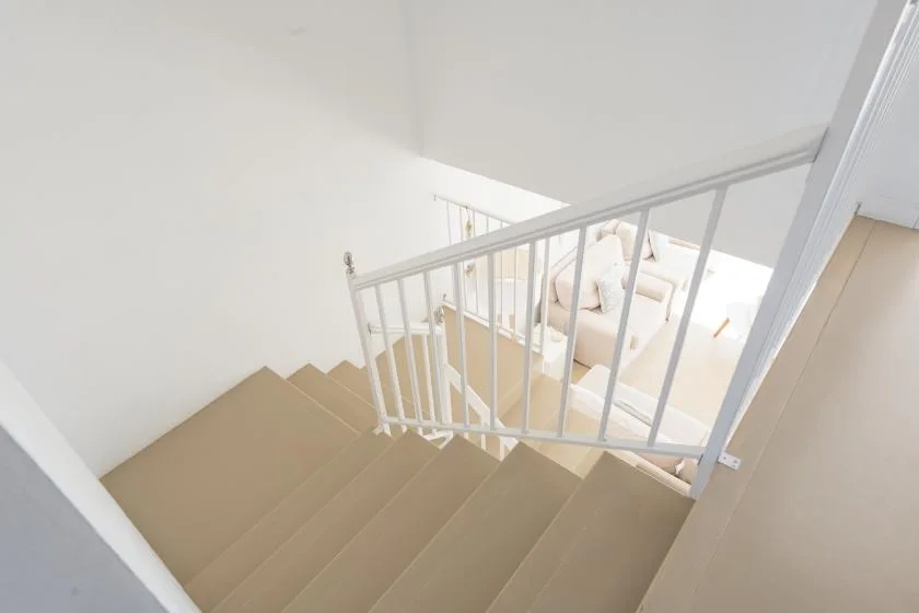 A staircase descends to a bright living area with seating.