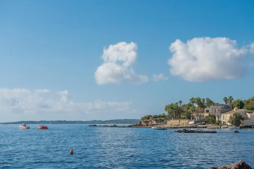 A coastal waterfront with calm blue water, small boats, and buildings along the shore.