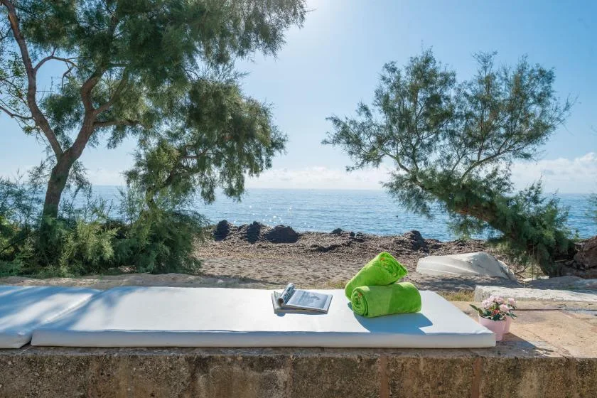 A seaside lounging area with a cushion and rolled towels overlooking the water.