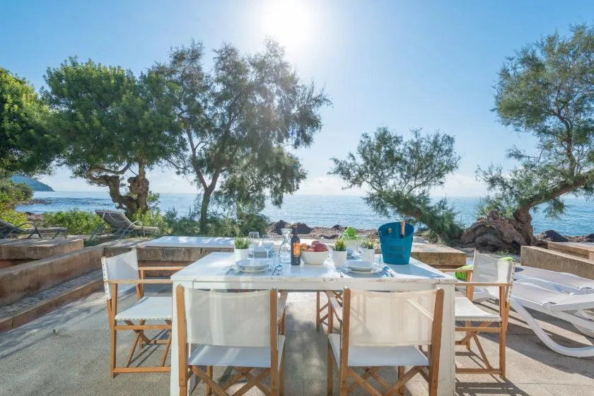 An outdoor dining area overlooks the sea, with a table set beneath the trees.