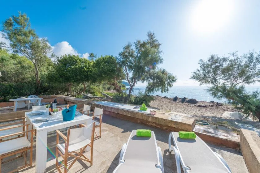 Outdoor dining tables and lounge chairs overlook a sunny beach and the sea.