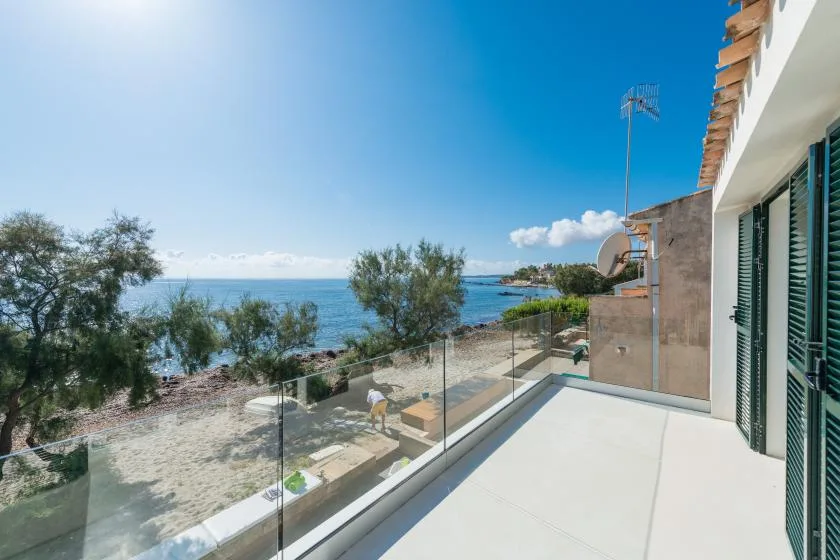 A seaside balcony with glass railing overlooks the water and shoreline.