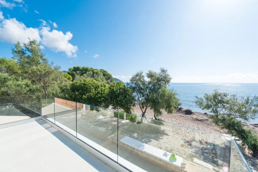 A glass-railed terrace overlooks trees and the shoreline beside the sea.