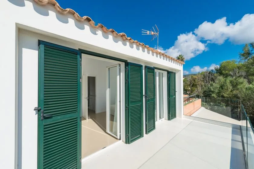 A sunny terrace beside a white building with green shutters and open glass doors.