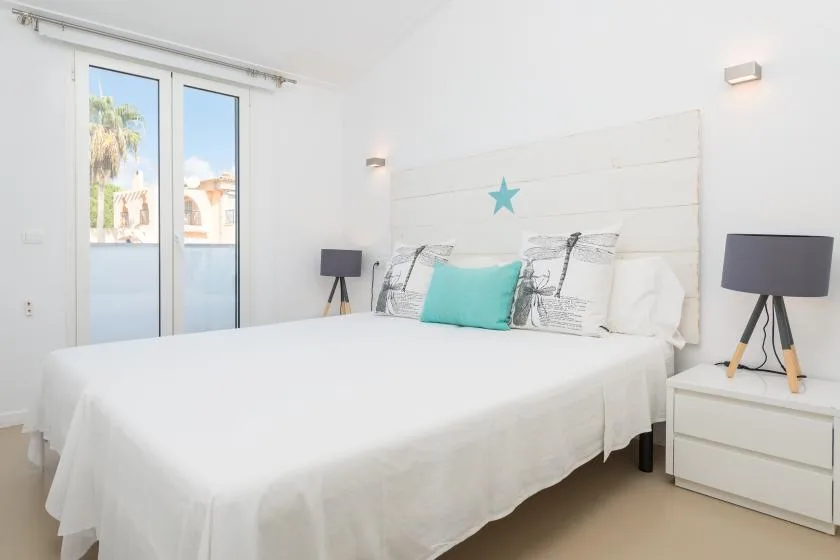 A bright bedroom with a white bed and turquoise accent pillow.
