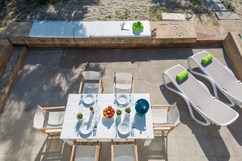 An outdoor dining table with place settings sits beside loungers on a paved patio.