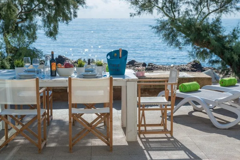 An outdoor dining table and lounge chairs sit beside the sea.