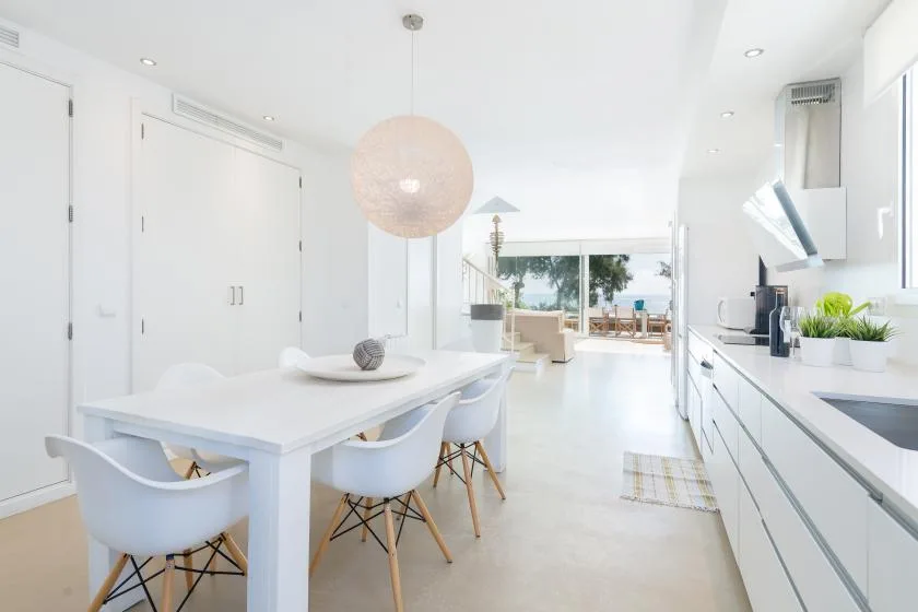 A bright dining area opens onto a living space, with a white table and kitchen counter.