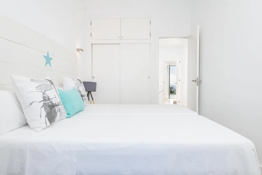 A bright bedroom with a white bed and an open doorway.