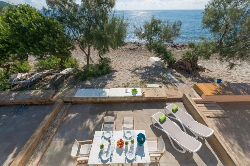 A seaside patio with a dining table, lounge chairs, and a view of the water.