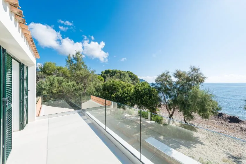 A seaside terrace overlooks the water, with a glass railing and nearby trees.