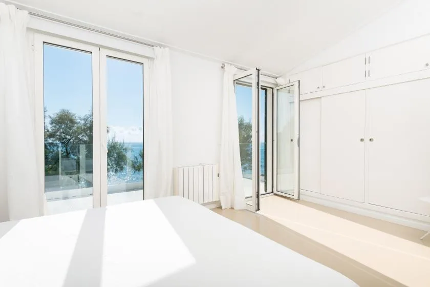 A bright bedroom with large windows and an open glass door overlooking the water.