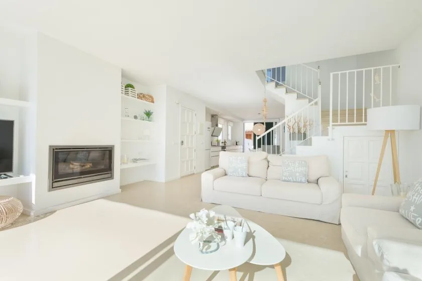 A bright living room with white seating, a coffee table, and a staircase.