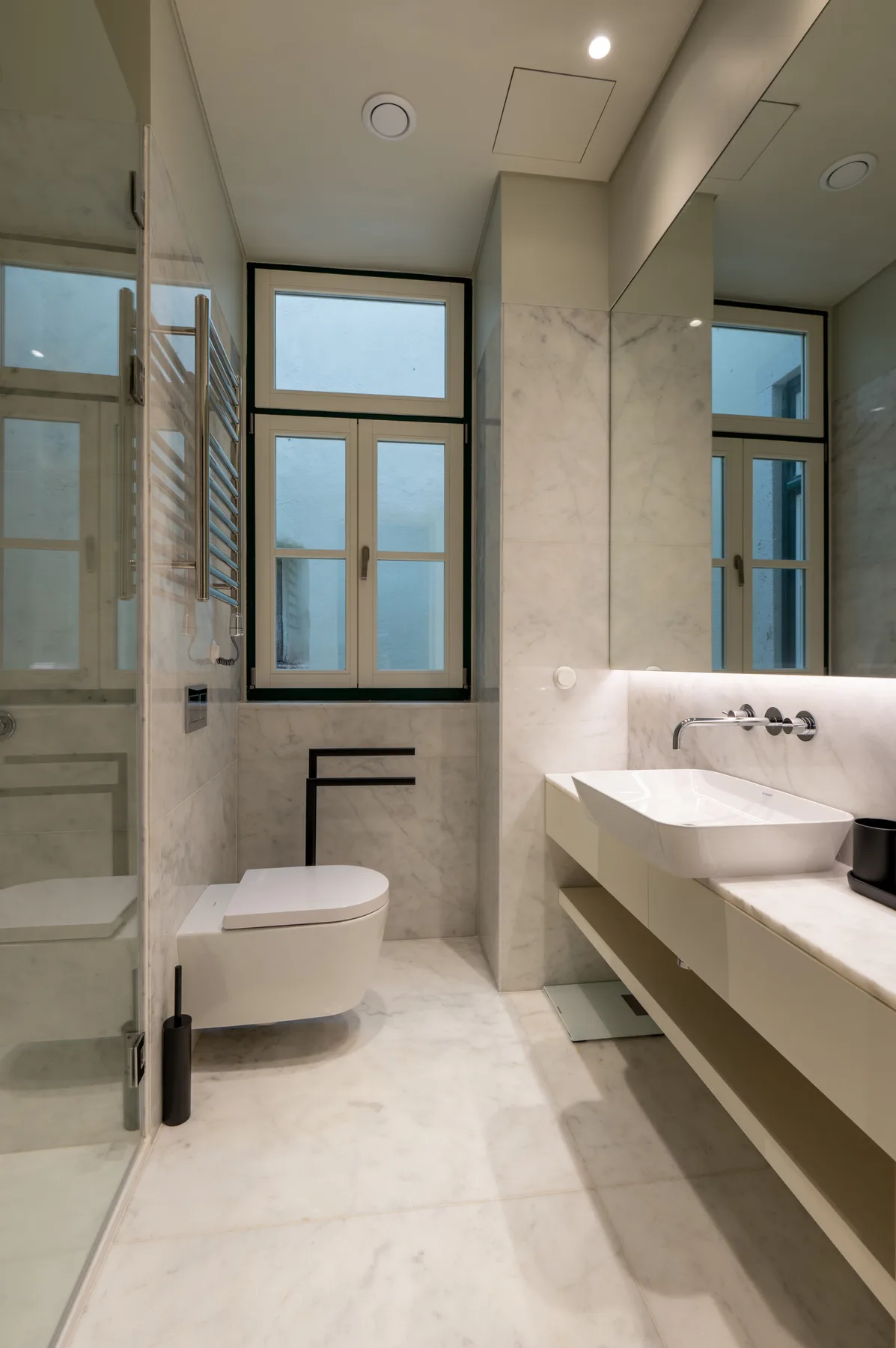 A bright bathroom with a walk-in shower, toilet, and wall-mounted sink.