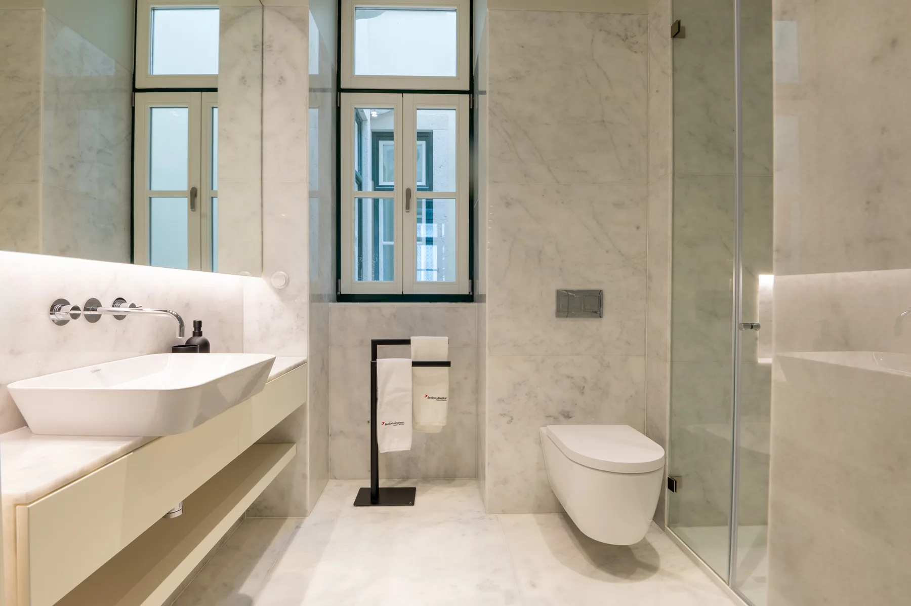 A bright bathroom with a sink, wall-mounted toilet, and glass shower.