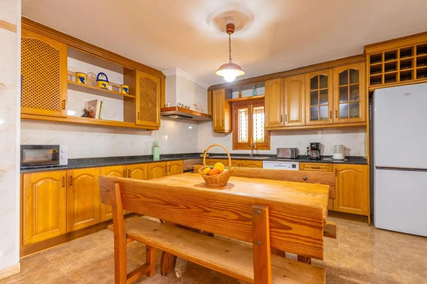 A kitchen with wooden cabinets and a large wooden table in the center.