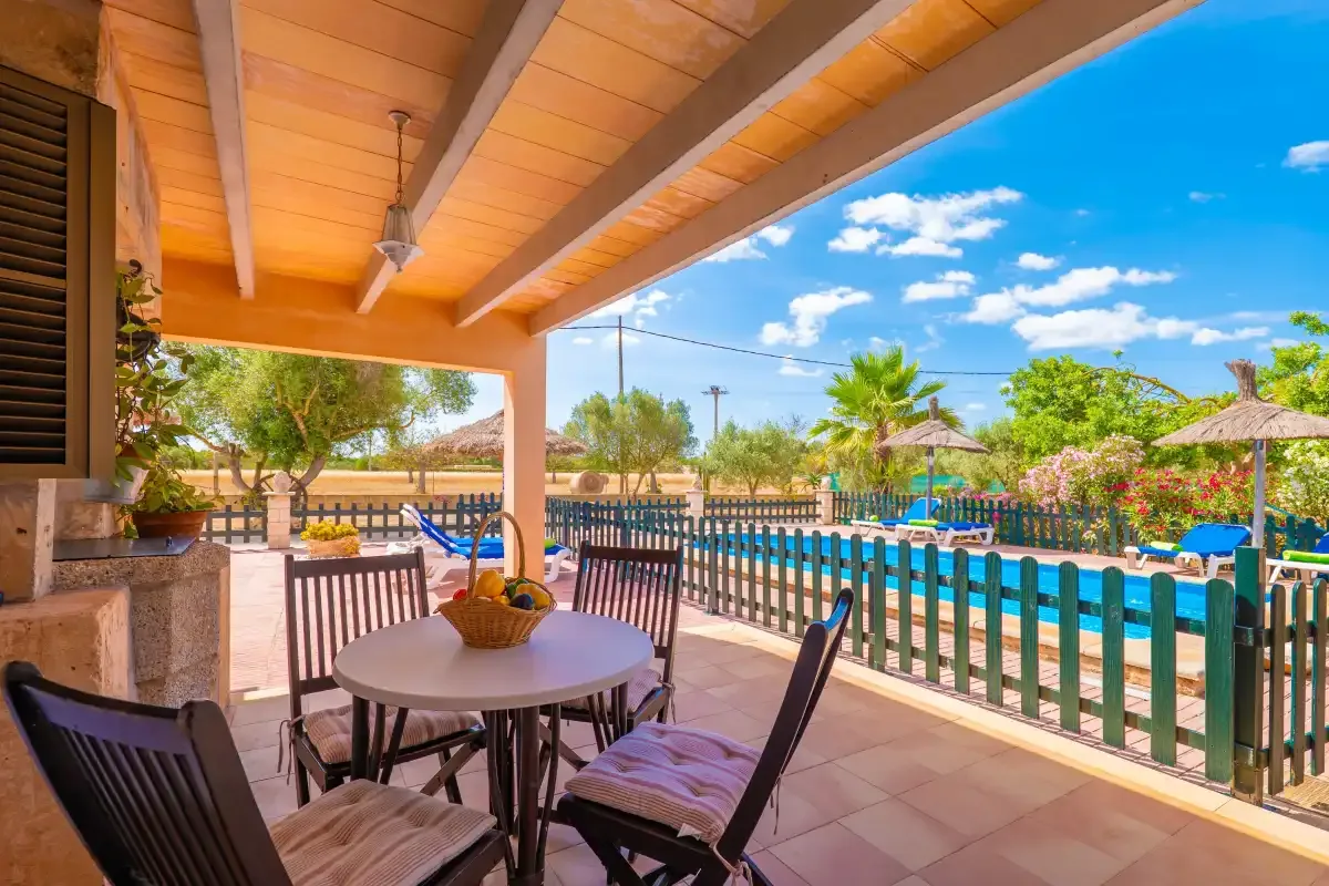 A covered patio with outdoor seating overlooks a swimming pool and garden.