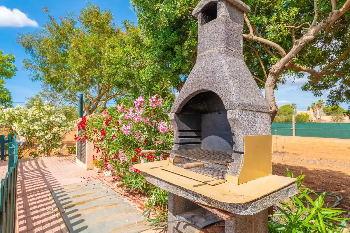 An outdoor barbecue area with a stone grill beside flowering plants.