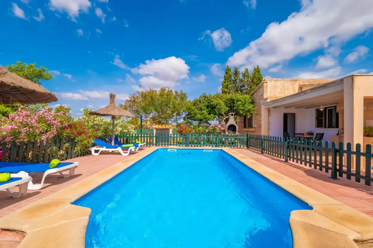 An outdoor swimming pool sits beside a covered patio and garden.