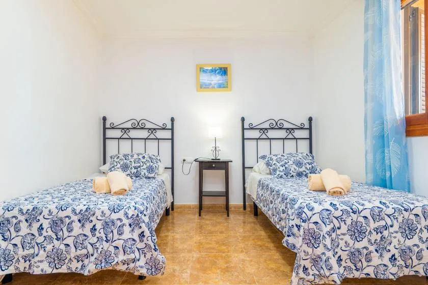 A bedroom with two beds featuring blue floral bedding and a small table between them.