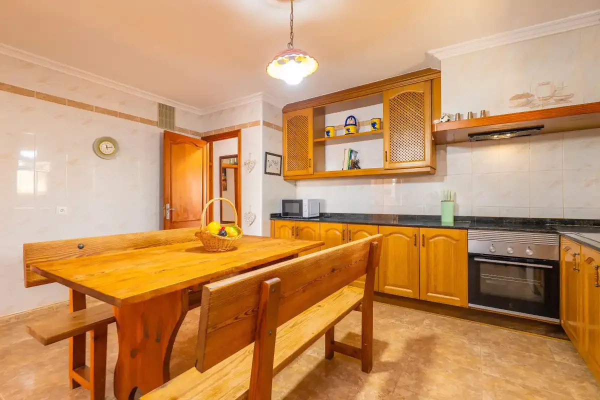 A kitchen with wooden cabinets, a dining table, and benches.