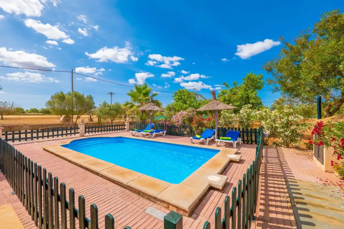 An outdoor swimming pool is surrounded by a paved deck and greenery.