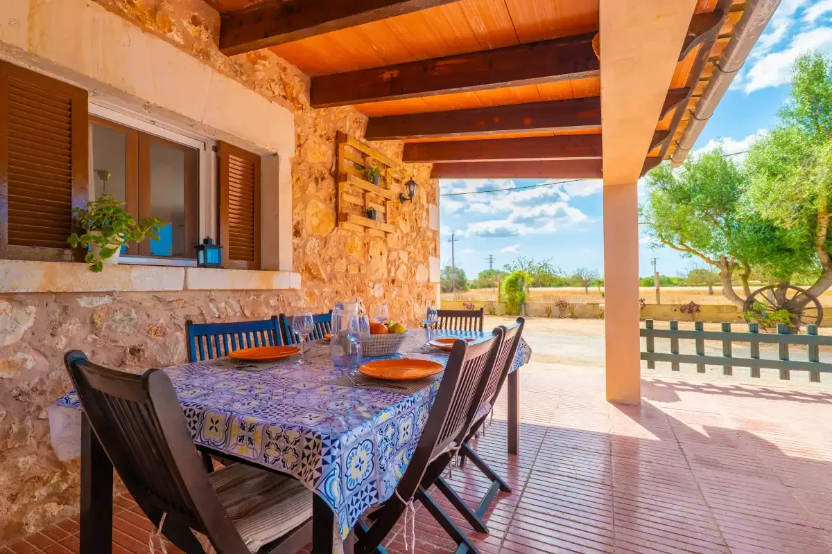 A covered outdoor dining area has a patterned table beside a stone wall.