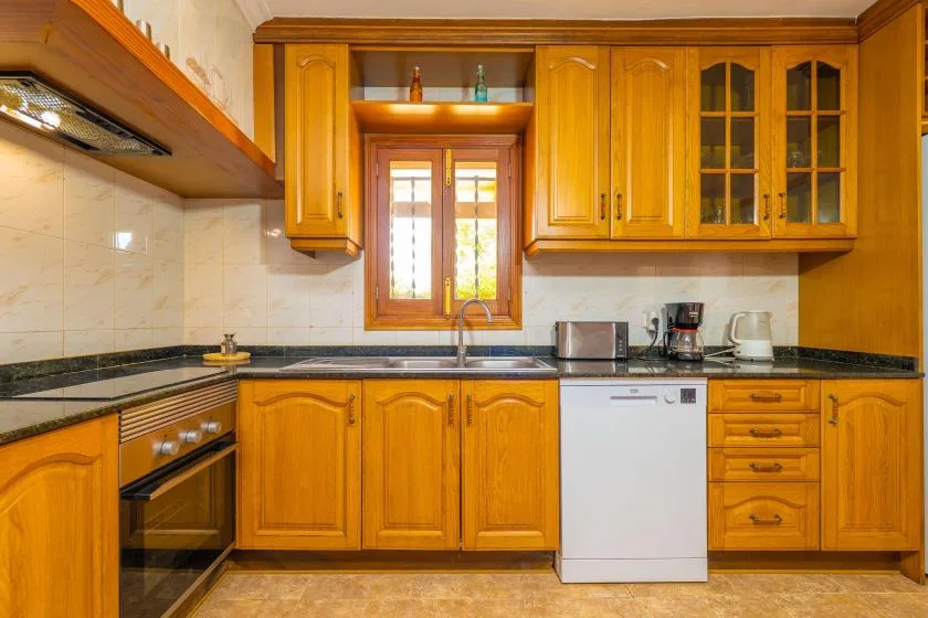 A warm-toned kitchen with wooden cabinets, a countertop, and a window above the sink.