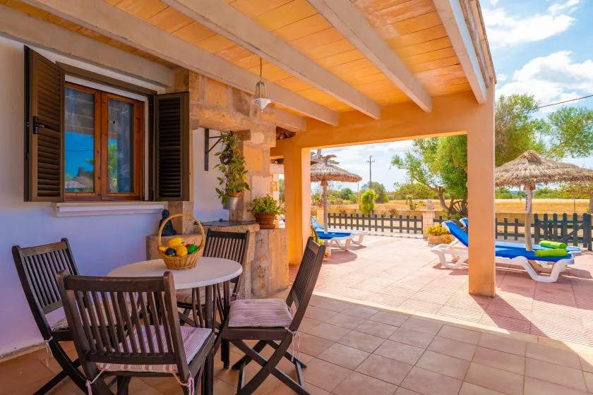 A covered patio has a dining table and seating overlooking a swimming pool.