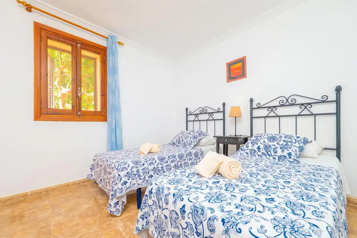 A bedroom with two beds, patterned bedding, and a wooden-framed window.