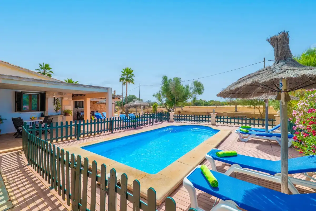 A swimming pool beside a patio with lounge seating and a thatched umbrella.