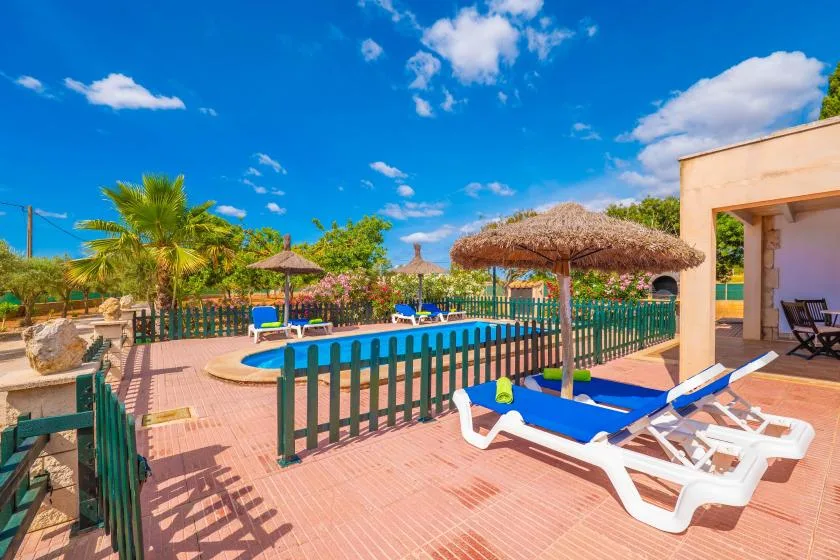 An outdoor pool area with blue lounge chairs and thatched parasols.