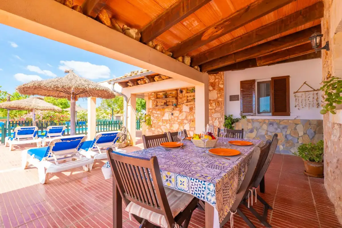 A covered outdoor dining area with a table beside a pool and sun loungers.
