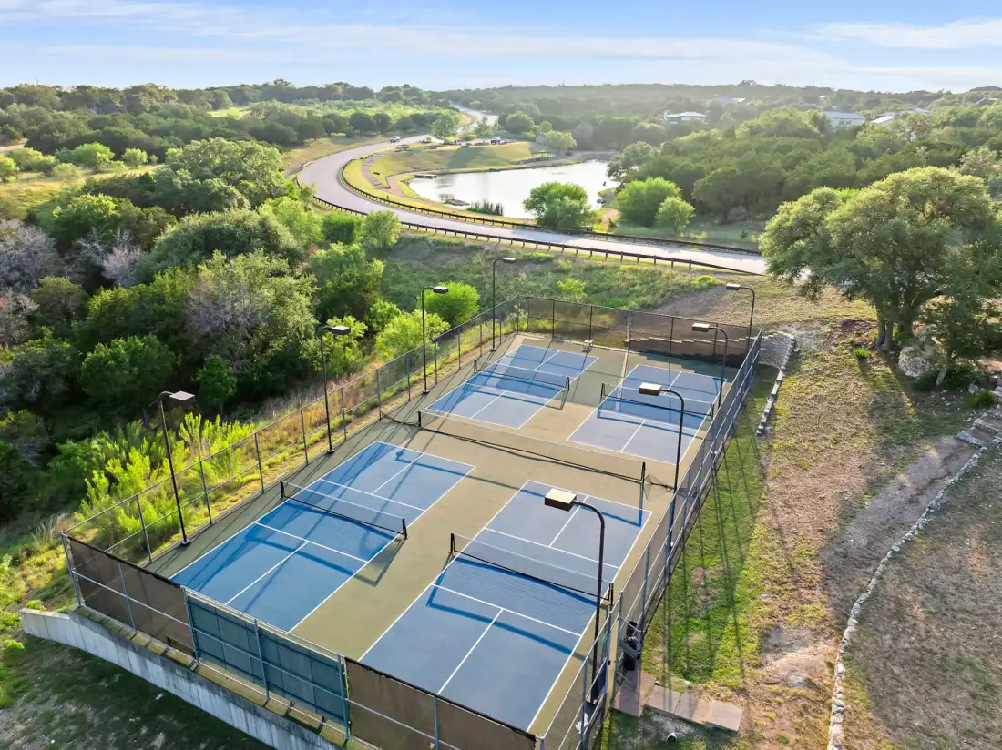 Aerial view of two outdoor tennis courts surrounded by lush greenery and a winding road near a river.