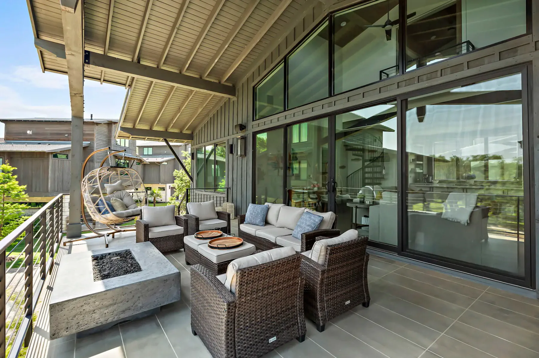 A covered patio has outdoor seating beside large glass doors and a hanging chair.