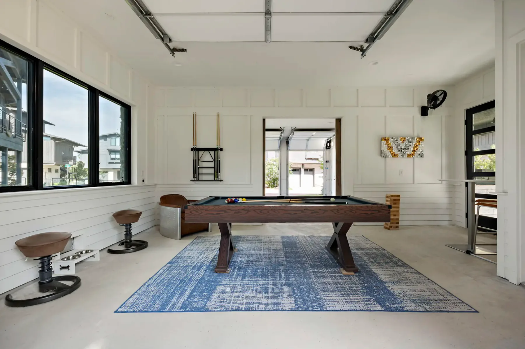 A game room with a billiard table on a blue rug and seating along the walls.